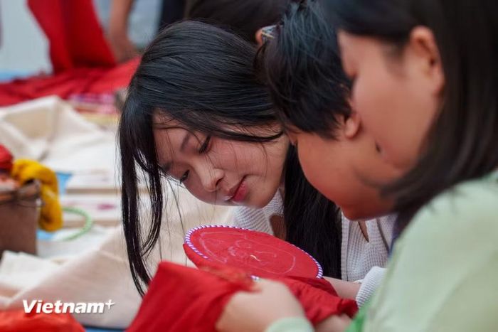 Các bạn trẻ chăm chút từng đường kim mũi chỉ trên nền lụa đỏ, cùng kết nối với di sản nghề dệt may thủ công truyền thống xứ Quảng. (Ảnh: Thanh Phong/Vietnam+)