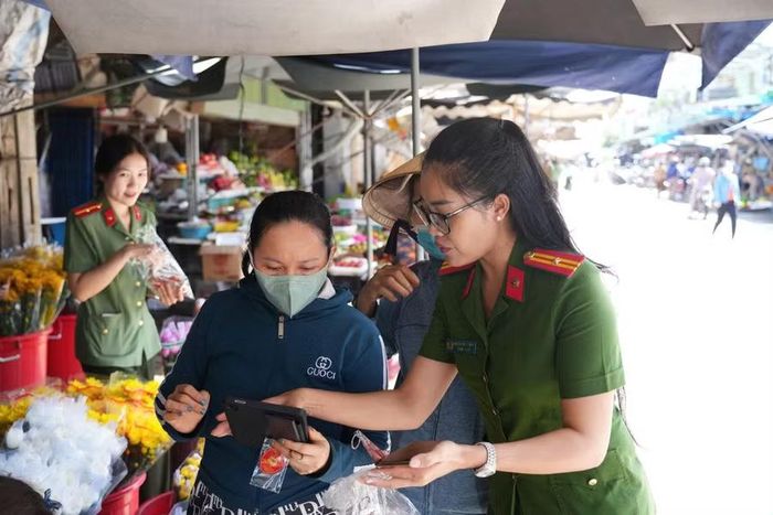 Cán bộ công an phường Tam Quan trao tặng móc khóa và hướng dẫn các hộ kinh doanh và người dân cách quét mã, truy cập. Ảnh: Thái Ngân
