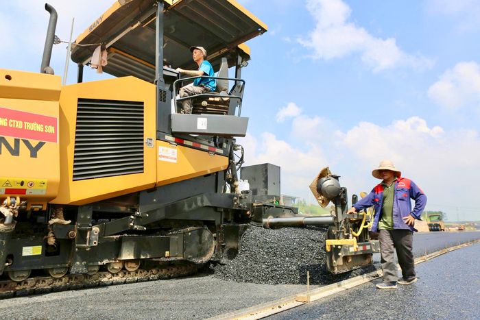 Ghi nhận tại đoạn tuyến qua phường Chơn Thành (TP Đồng Nai), nhiều dây chuyền thảm bê tông nhựa đang hoạt động liên tục. Máy rải nhựa, lu rung, lu bánh thép cùng các thiết bị chuyên dụng nối tiếp nhau triển khai, từng bước hình thành lớp mặt đường cao tốc.