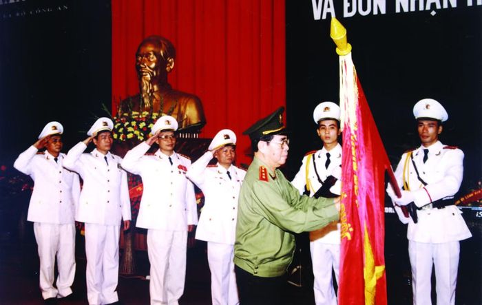  Thượng tướng Lê Minh Hương, Ủy viên Bộ Chính trị, Bộ trưởng Bộ Công an gắn Huân chương Lao động hạng Ba lên Cờ truyền thống của Báo CAND (ngày 1/11/2001). 
