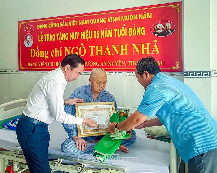Đồng chí Phan Thanh Duy, Ủy viên Ban Thường vụ Tỉnh ủy, Trưởng Ban Tổ chức Tỉnh ủy (bìa trái) và đồng chí Võ Văn Đa, Phó Bí thư Trường trực Đảng ủy phường An Xuyên, trao Huy hiệu 65 năm tuổi Đảng đến đồng chí Ngô Thanh Nhã.